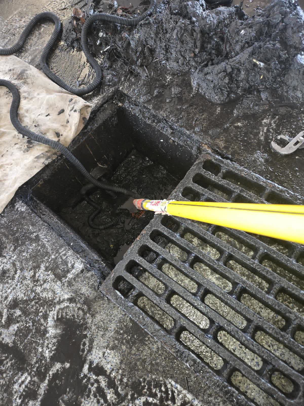 A commercial trench drain with the grate pulled aside, cable and jetter rod feeding in.