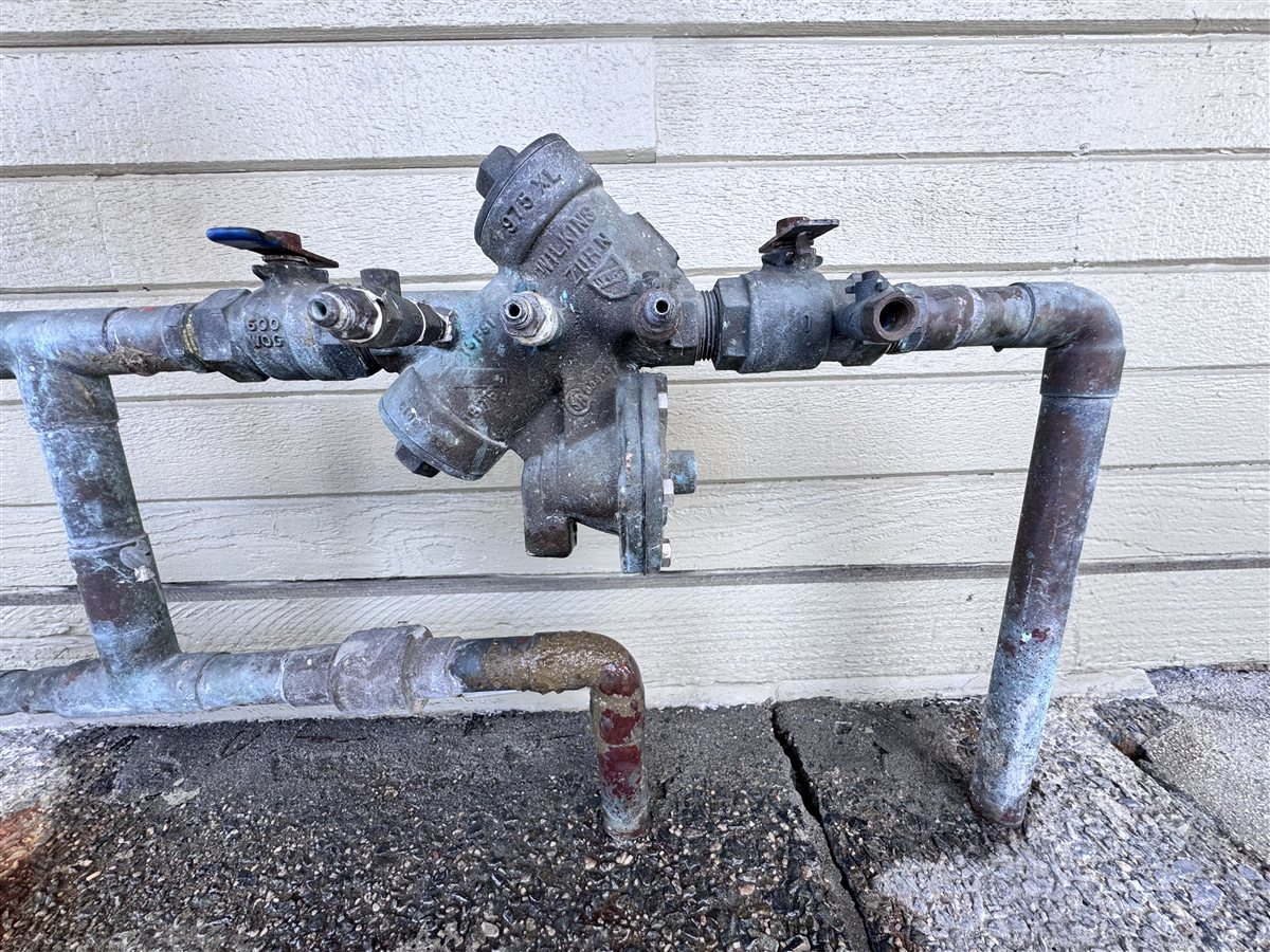 Corroded backflow preventer assembly on an Imperial Beach exterior wall.