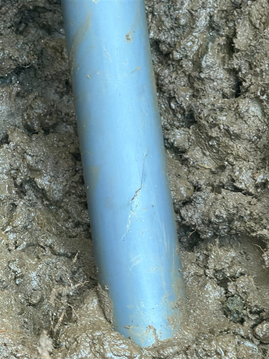 Cracked water service line exposed in a trench.