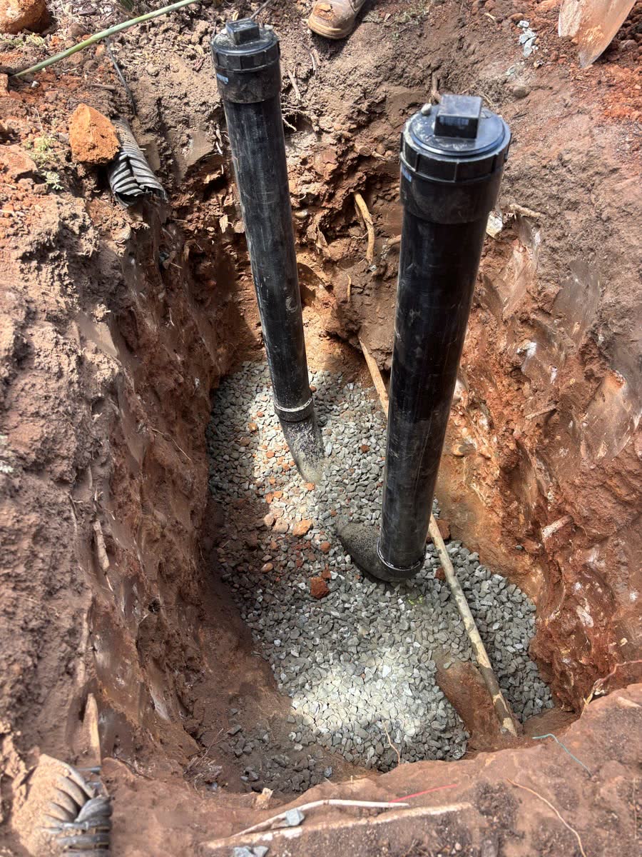 Two new sewer cleanout risers set on gravel in a deep hand dug excavation.